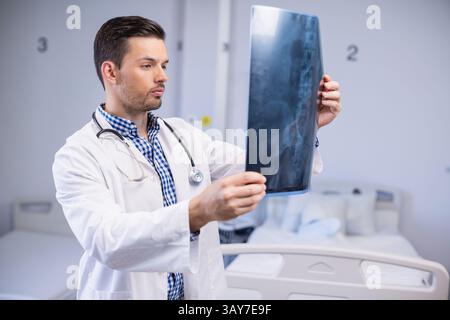 Médecin chinois examinant un film radiographique dans une chambre d'hôpital avec stéthoscope, linge de lit, espace de copie Banque D'Images