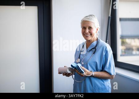 Infirmière principale tenant un tensiomètre et un brassard à la fenêtre de la clinique, espace copie Banque D'Images
