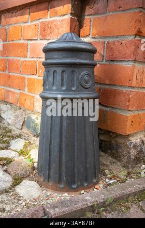 Une bouche d'incendie noire est assise sur le sol à côté d'un mur de briques. La bouche d'incendie est vieille et rouillée, et elle est entourée de saleté et de débris Banque D'Images