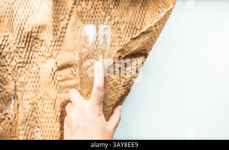 Quelqu'un emballe un verre dans un papier d'emballage marron écologique pour le déménagement. Verre d'emballage pour post-livraison. Banque D'Images
