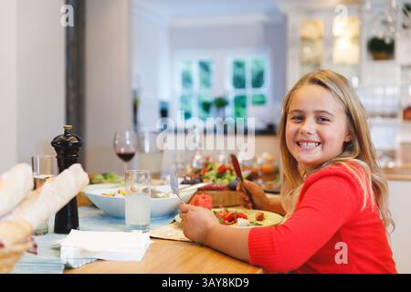 Fille de sept ans assise à la table à manger dans la cuisine, avec saladier, petits pains, espace copie Banque D'Images