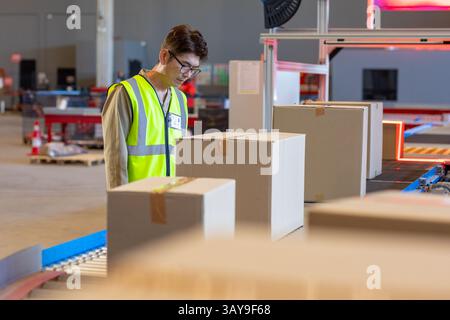 Homme coréen inspectant des boîtes sur la bande transporteuse dans l'entrepôt, avec machines de numérisation, espace de copie Banque D'Images
