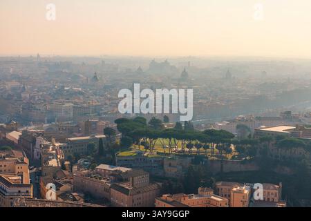 Vue aérienne brumeuse du paysage urbain de Rome avec des dômes historiques et des bâtiments sous la lumière douce du soleil au lever du soleil, vue depuis la cité du Vatican, Italie. Voyages populaires Banque D'Images