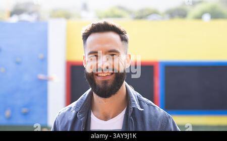 Homme adolescent debout à l'aire de jeux par des panneaux muraux colorés, portant une chemise en denim et un T-shirt blanc Banque D'Images