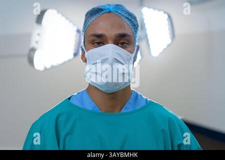 Homme professionnel debout dans la salle d'opération sous des lumières LED, portant une blouse chirurgicale, un chapeau et un masque Banque D'Images