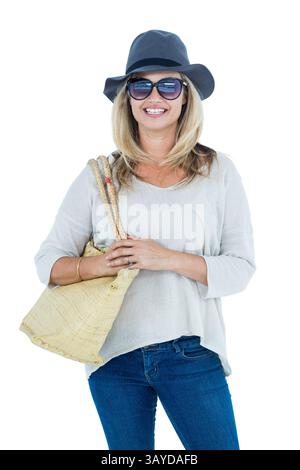 Femme d'âge moyen debout et souriante dans un cadre de studio intérieur, avec chapeau de soleil et sac fourre-tout en paille Banque D'Images