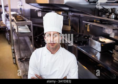 Chef masculin portant manteau et chapeau, travaillant dans la cuisine commerciale avec des fours en acier et des cuisinières Banque D'Images