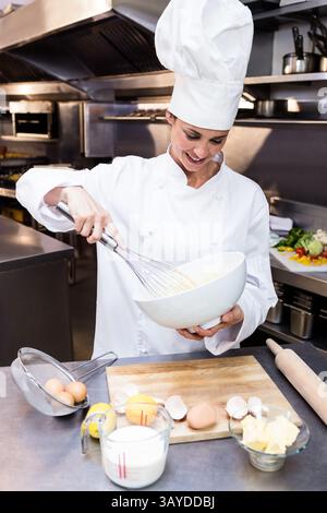 Chef cuisinier senior mélangeant la pâte dans la cuisine commerciale, avec fouet en métal et grand bol à mélanger Banque D'Images