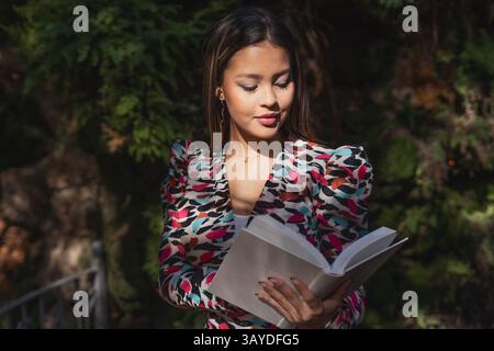 Une jeune femme à la mode paisiblement immergée dans la lecture en plein air, mettant magnifiquement en valeur son style et sa sérénité Banque D'Images