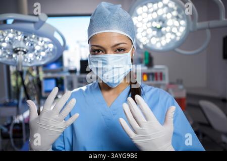 Chirurgien féminin portant des gants et un capuchon de récurage dans la salle d'opération, avec plafonniers et moniteurs Banque D'Images
