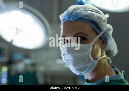 Chirurgien féminin souriant avec les yeux dans la salle d'opération, avec masque et lumières LED plafonnières, espace de copie Banque D'Images