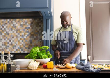 Homme afro-américain senior hachant des champignons sur le comptoir dans la cuisine moderne, espace de copie Banque D'Images