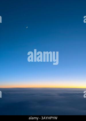 Croissant de lune dans le ciel bleu profond au coucher du soleil vu à travers la fenêtre de l'avion Banque D'Images