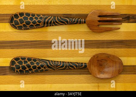 Salade africaine traditionnelle décorative en bois sculptée à la main, cuillère et fourchette sur une planche à découper en bois dur de noix, châtaignier et cerisier Banque D'Images