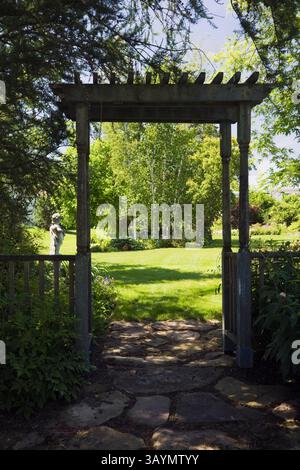 Chemin de dalles à travers la tonnelle en bois silhouette menant à une pelouse d'herbe verte baignée de soleil avec Betula - bouleaux dans le jardin de l'arrière-cour au printemps. Banque D'Images