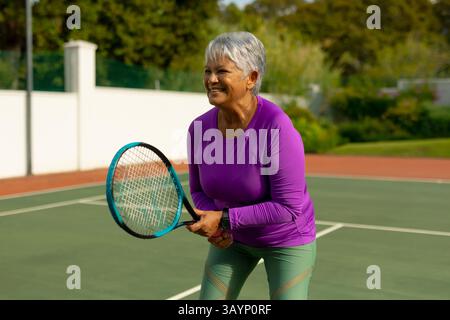 Femme senior debout prêt sur le court de tennis, tenant la raquette, portant smartwatch, espace de copie Banque D'Images