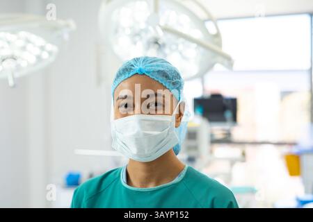 Femme afro-américaine debout dans la salle d'opération de l'hôpital, avec des lumières chirurgicales et des moniteurs Banque D'Images