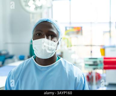 Chirurgien afro-américain debout dans la salle d'opération, portant une casquette chirurgicale et un masque bleus de gommage Banque D'Images