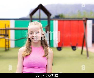 Fille de huit ans souriant à l'aire de jeux pour enfants avec cadre d'escalade en bois et balançoires noires Banque D'Images