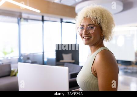 Jeune femme utilisant un ordinateur portable et portant des lunettes à cadre transparent dans le salon de bureau, espace de copie Banque D'Images