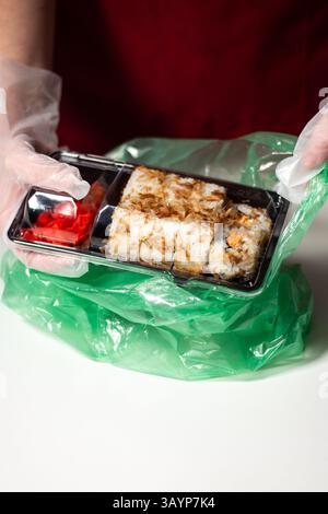 Concept sushi to Go. Emportez la boîte avec des rouleaux de sushi dans les mains de la femme dans les gants. Concept de livraison de nourriture. Concept de nourriture à emporter. Banque D'Images