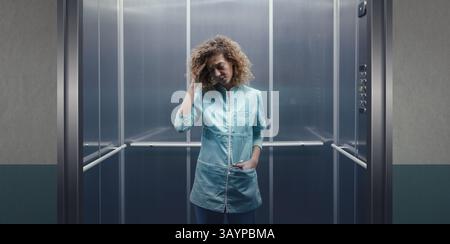Médecin féminin fatigué stressé debout dans l'ascenseur et touchant sa tête, elle a mal à la tête Banque D'Images