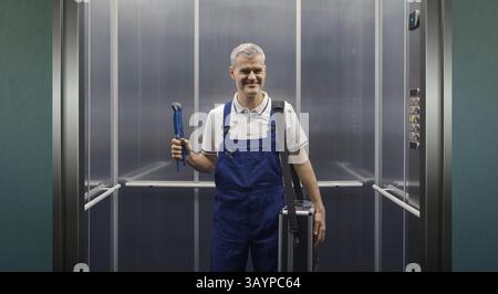 Portrait d'un plombier professionnel souriant debout dans un ascenseur et tenant des outils de travail Banque D'Images