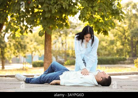 Jeune femme faisant la RCP à un mari inconscient ayant une crise cardiaque dans la rue Banque D'Images