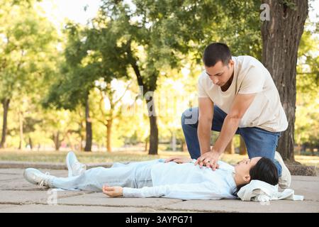 Jeune homme faisant la RCP sur une femme inconsciente ayant une crise cardiaque dans le parc Banque D'Images