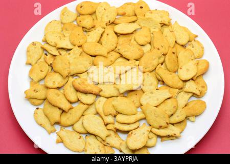 Savoureux biscuits en forme de poisson dans une plaque blanche gros plan sur un fond cramoisi Banque D'Images