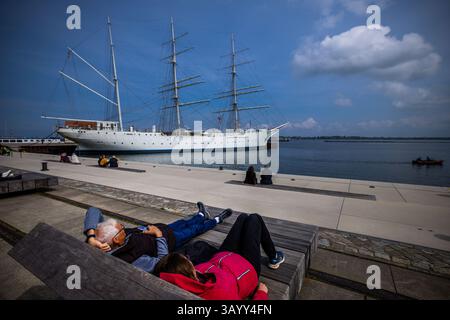 Stralsund, Allemagne. 23 avril 2025. Les vacanciers profitent du temps ensoleillé dans le port de la ville devant le voilier « Gorch Fock I » pour une pause détente. Le navire-école, qui a été construit pour la marine allemande, a été lancé à Hambourg en 1933 et est allé en Union soviétique en réparation après la fin de la guerre. En 2003, l'association 'Tall Ship Friends' a acquis le navire de l'Ukraine et l'a amené à Stralsund. Crédit : Jens Büttner/dpa/Alamy Live News Banque D'Images
