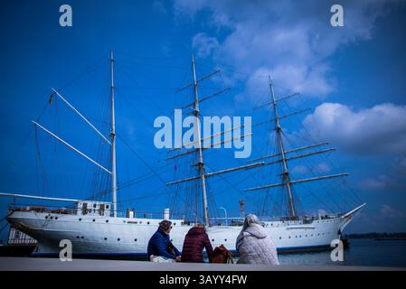 Stralsund, Allemagne. 23 avril 2025. Les vacanciers profitent du temps ensoleillé dans le port de la ville devant le voilier « Gorch Fock I » pour une pause détente. Le navire-école, qui a été construit pour la marine allemande, a été lancé à Hambourg en 1933 et est allé en Union soviétique en réparation après la fin de la guerre. En 2003, l'association 'Tall Ship Friends' a acquis le navire de l'Ukraine et l'a amené à Stralsund. Crédit : Jens Büttner/dpa/Alamy Live News Banque D'Images