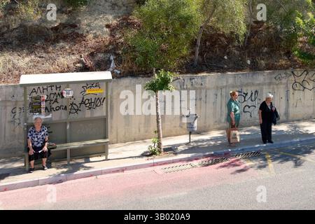 Crète. Grèce - 23 avril 2025 : arrêt de bus en milieu urbain avec abri couvert, banc et marquage des rues. Les gens attendent, entourés de graf Banque D'Images