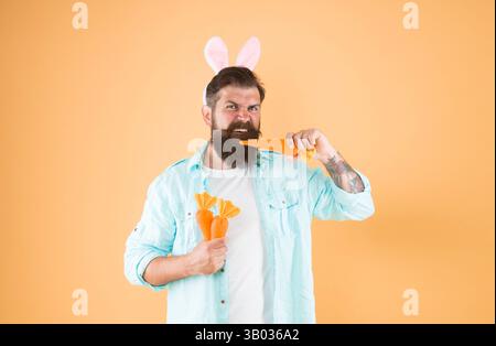 Faits nutritionnels et bienfaits pour la santé. La carotte se compose de vitamines. Heureux et en bonne santé. Le lapin de Pâques tient des carottes. Les oreilles de lapin d'homme barbu tiennent les légumes Banque D'Images