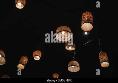 Lampes suspendues en rotin tissé avec lumières chaudes et plafond sombre Banque D'Images