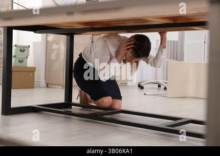 Une jeune femme effrayée se cachant sous le bureau pendant le tremblement de terre Banque D'Images