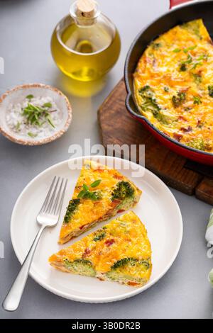 Frittata de brocoli, bacon et fromage cuit dans une poêle en fonte avec deux tranches sur une assiette Banque D'Images