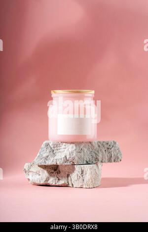 Pot de bougie rose avec couvercle en bois debout sur des pierres grises sur fond rose. Banque D'Images