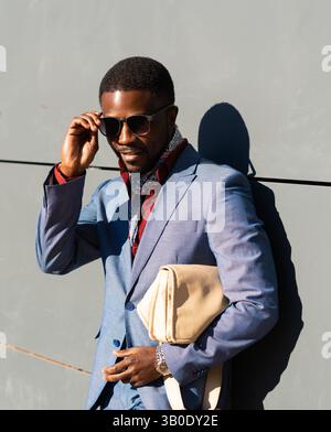 Un professionnel élégant vêtu d'un costume bleu, avec des lunettes de soleil et un sac fourre-tout Banque D'Images