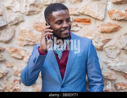 Un homme élégant habillé dans un costume bleu Sharp heureux engagé dans une conversation téléphonique Banque D'Images