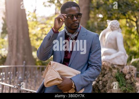 Un homme élégant vêtu d'une tenue élégante portant des lunettes de soleil dans un cadre magnifique de parc Banque D'Images