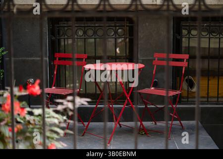 Table rouge vif avec deux chaises assorties sur un patio extérieur confortable. Image stock parfaite pour manger, détente, design urbain, culture de café, romantique Banque D'Images