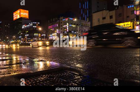 Busan, Corée du Sud - 19 mars 2018 : scène nocturne urbaine mettant en vedette les rues de la ville illuminées par des panneaux au néon vibrants et des feux de véhicules reflétés sur le p humide Banque D'Images