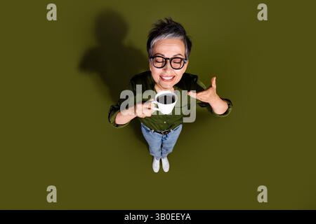 Femme élégante dans une tenue décontractée profitant d'une tasse de café sur un fond kaki mettant en valeur un style de vie joyeux et élégant, vue de dessus Banque D'Images