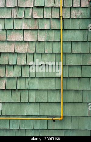 tuyau d'évacuation rouillé jaune fixé ou fixé à l'extérieur extérieur du mur de bardeaux ou de shake peint en vert décoloration et écaillage rustique texturé Banque D'Images