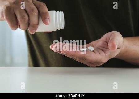 Un homme tient une bouteille de pilules et une bouteille de pilules. Il verse les pilules dans sa main Banque D'Images