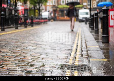 Proche focalisé London Soho rue pavée avec une personne portant un parapluie en arrière-plan et un espace pour copier le texte Banque D'Images