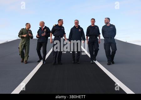 (Gauche-droite) Capitaine Colin McGannity (RN) commandant du groupe aérien de transport, le secrétaire à la Défense John Healey, le commodore James Blackmore commandant du groupe d'attaque de porte-avions, le premier ministre Sir Keir Starmer, le vice-amiral Andy Burns commandant de la flotte et le capitaine Will Blackett capitaine du HMS Prince of Wales marchent sur la rampe de décollage du HMS Prince of Wales, le porte-navire phare de la Royal Navy, à Plymouth, dans le Devon, avant un déploiement de huit mois dans la région Indo-Pacific HighMast. Le navire, qui a quitté Portsmouth mardi, se rendra en Méditerranée, Middle E. Banque D'Images