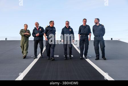 (Gauche-droite) Capitaine Colin McGannity (RN) commandant du groupe aérien de transport, le secrétaire à la Défense John Healey, le commodore James Blackmore commandant du groupe d'attaque de porte-avions, le premier ministre Sir Keir Starmer, le vice-amiral Andy Burns commandant de la flotte et le capitaine Will Blackett capitaine du HMS Prince of Wales marchent sur la rampe de décollage du HMS Prince of Wales, le porte-navire phare de la Royal Navy, à Plymouth, dans le Devon, avant un déploiement de huit mois dans la région Indo-Pacific HighMast. Le navire, qui a quitté Portsmouth mardi, se rendra en Méditerranée, Middle E. Banque D'Images