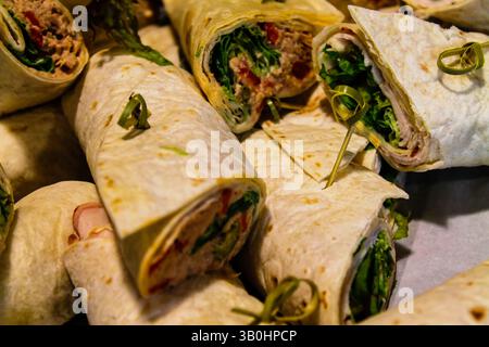 Une vue rapprochée de roulés remplis de légumes verts, de viandes et de pâtes à tartiner, disposés sur une surface. Les wraps sont soigneusement roulés et garnis de HE vert Banque D'Images